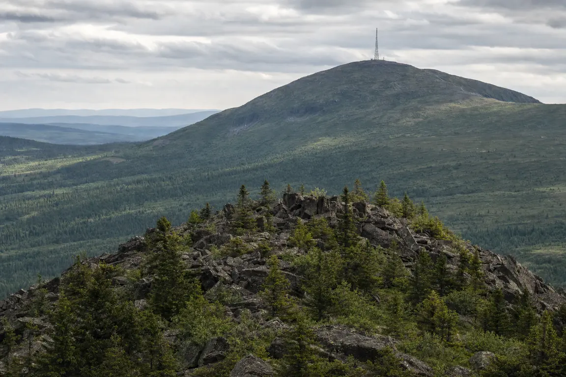 Blockhalde auf einer freistehenden Kuppe mit Blick auf einen größeren Berg mit Sendemast