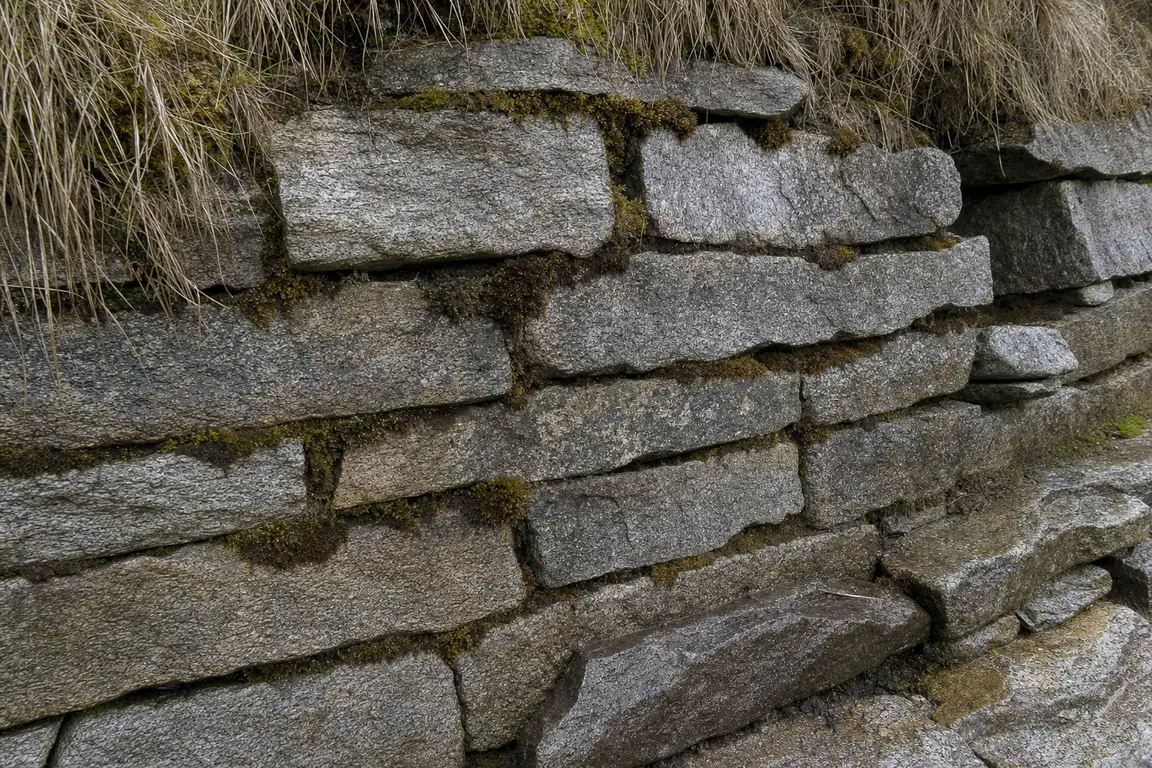 Nahaufnahme einer mörtellos gesetzten Trockenmauer aus Granitplatten mit Moos in den Fugen