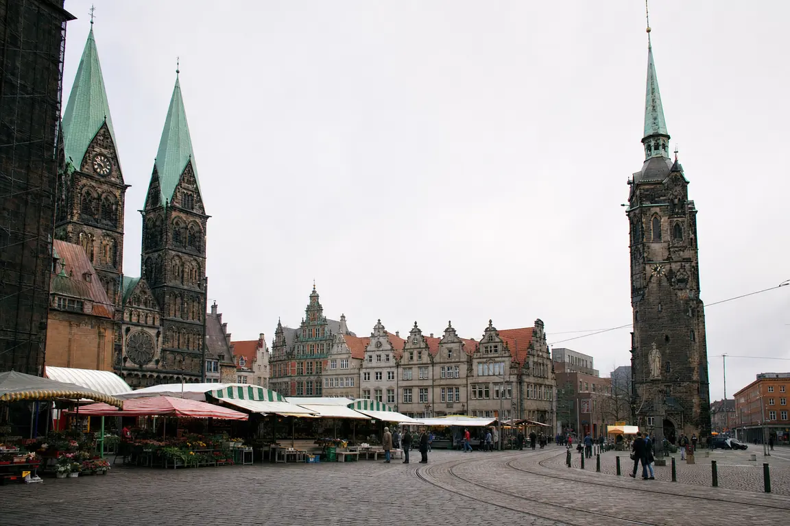 Großer städtischer Marktplatz mit hohen Kirchtürmen und einem freistehenden schlanken Turm